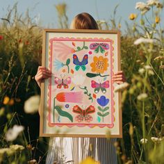 a woman holding up a painting in the middle of a field with wildflowers