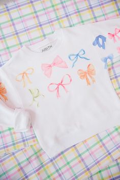 Perfect for Easter egg hunts and springtime adventures, our MINI KIDS BOW PRINT PULLOVER adds a pop of playful style to any outfit. The white pullover features a charming print of pastel colored bows, making it a delightful addition to your little one's wardrobe. Time to hop to it! This is a made-to-order item. All customized orders are currently shipping within 14 business days. To receive item quicker, expedited shipping is available at checkout. Playful Tops For School In Spring, Playful Spring Tops For School, Preppy Multicolor Tops For Spring, Cute Pastel Cotton Top, Preppy White Top For Spring, Cute Pastel Tops For Spring, White Preppy Top For Spring, Casual White Tops With Bow, Playful Pastel Tops For Spring