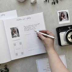 a person holding a pen next to an open book with photos on it and a camera