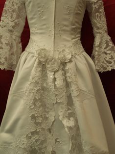 a white wedding dress with flowers on the waist and sleeves, is displayed in front of a red background