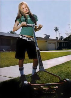 a woman standing on top of a scooter in front of a house with grass