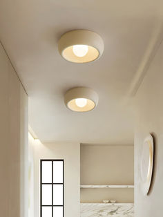 three circular lights are hanging from the ceiling in this modern bathroom with white walls and marble flooring