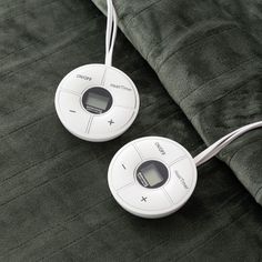 two electronic devices sitting on top of a green bed sheet with corded plugs