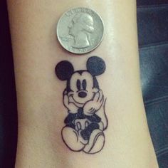 a small mickey mouse tattoo on the ankle with a penny sitting next to it's side