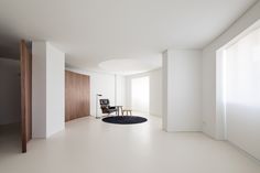 an empty white room with a chair and rug on the floor in front of it