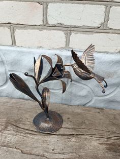 two metal birds sitting on top of a wooden table next to a white brick wall