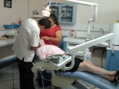 a woman is getting her teeth checked at the dentist's office while two men look on