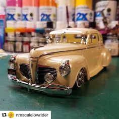 an old model car is sitting on the table in front of some paint bottles and cans