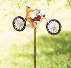 a statue of a man riding a motorcycle on top of a wooden pole in the grass