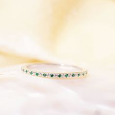 a close up view of a ring on a white surface with green and white stones