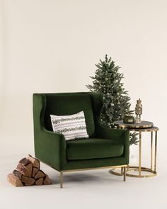 a green chair next to a small christmas tree in front of a white wall with a gold side table