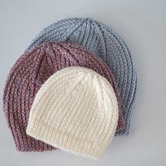 three knitted hats are shown on a gray background, one is white and the other is blue