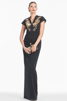 a woman wearing a black dress with gold embroidered details on the shoulders and neckline