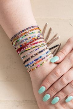 a woman's hand with several different colored bracelets on top of her arm