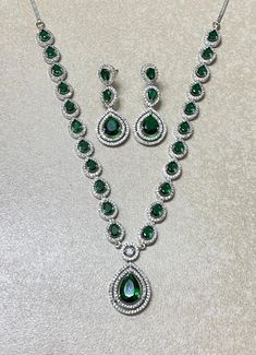 Emerald Diamond Necklace features a striking green faux emerald pendant surrounded by sparkling American diamonds and cubic zirconia. The statement piece reflects the elegance of Indian and Pakistani jewelry, making it a beautiful and culturally rich gift for her. Perfect for special occasions, this jewelry set adds a touch of luxury and timeless beauty to any collection. *𝐏𝐑𝐎𝐃𝐔𝐂𝐓 𝐃𝐄𝐓𝐀𝐈𝐋* * 𝐌𝐚𝐭𝐞𝐫𝐢𝐚𝐥: Brass * 𝐏𝐥𝐚𝐭𝐢𝐧𝐠: White Rhodium Plated * 𝐒𝐭𝐨𝐧𝐞: AAA-quality CZ D Cubic Zirconia Necklace For Party, May Birthstone, Green Sparkling Stones Jewelry Sets For Party, Green Round Crystal Jewelry, Glamorous Green Jewelry For Formal Occasions, Green Jewelry Sets With Diamond Accents For Party, Green Crystal Jewelry Sets With Sparkling Stones, Green Stone Jewelry For Formal Occasions, Green Stone Formal Jewelry, Green Crystal Necklaces With Sparkling Stones