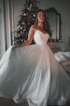 a woman in a white dress standing next to a christmas tree and holding her skirt