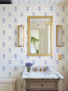 a bathroom with a mirror, sink and wallpaper in blue and white colors on the walls