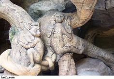 an elephant statue sitting on top of a pile of rocks next to a tree trunk