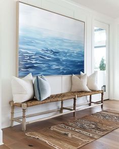 a painting is hanging on the wall above a bench in a room with hardwood floors