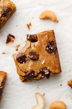 chocolate chip cookie bars with cashews and almonds scattered around them on a white surface