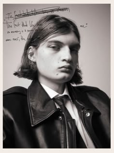 a young man wearing a leather jacket and tie with writing on the wall behind him