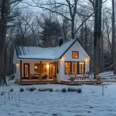 a small white house in the snow with lights on it's windows and porch