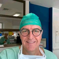 a man in scrubs and glasses is smiling at the camera