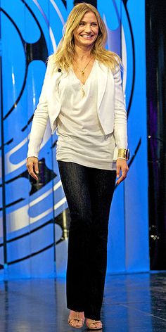 a woman is walking down the runway wearing black pants and a white jacket with an embellishment on her face