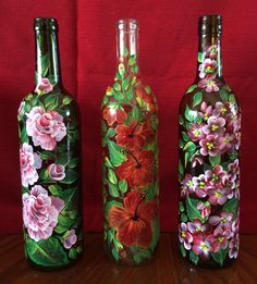 three painted wine bottles sitting on top of a wooden table next to a red wall