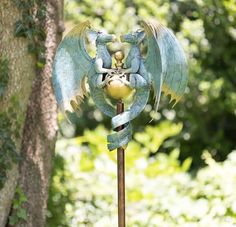 a blue bird statue on top of a metal pole next to a tree in the woods