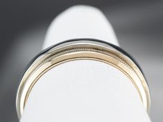 two tone gold and black wedding band on white fabric with grey background, closeup