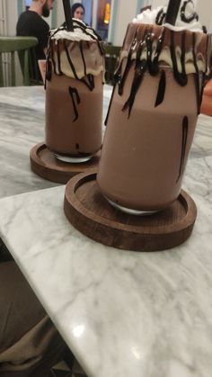 two chocolate desserts sitting on top of a marble table with people in the background