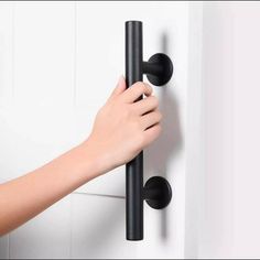 a person's hand is holding onto the handle of a black door handle on a white wall