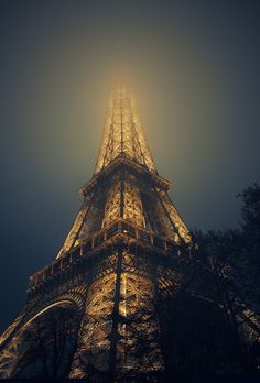 the eiffel tower lit up at night with its lights on and fog in the air