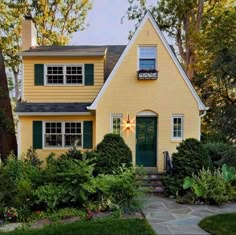 a yellow house with green shutters on the front and side windows is surrounded by greenery