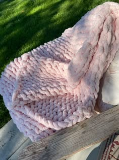 a pink blanket is laying on top of a wooden bench in front of some grass