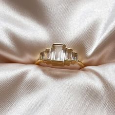 an engagement ring with three baguettes sitting on a white satin surface, close up