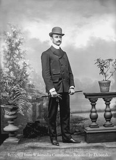 an old black and white photo of a man in a suit standing next to a potted plant