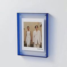 two women in white dresses standing next to each other on a wall with a blue frame