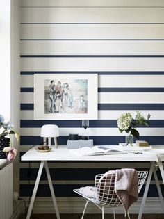 a white desk topped with a laptop computer next to a wall covered in striped walls