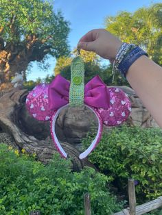 a person holding up a minnie mouse ears headband with pink and green flowers on it