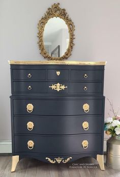 a blue dresser with gold accents and a mirror on the top, next to a potted plant