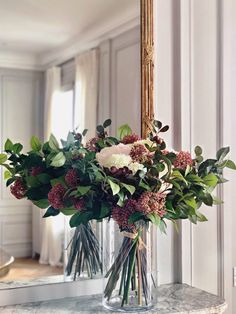 a vase filled with flowers sitting on top of a marble counter next to a mirror