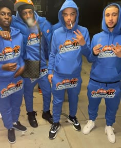 five young men in matching blue tracksuits posing for the camera with their fingers up