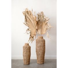 two vases with dried plants in them sitting on a concrete floor next to a white wall