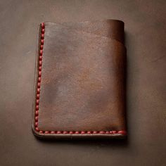 a brown leather wallet with red stitching on the outside and inside, sitting on a table