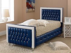 a blue bed with white headboard and foot board on carpeted floor next to window