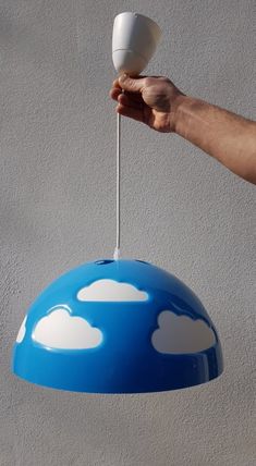 a hand holding a light fixture with clouds painted on it