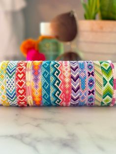 multicolored bracelets stacked on top of each other in front of a potted plant