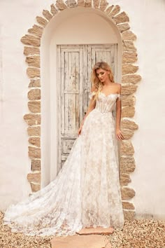 a woman standing in front of a door wearing a wedding dress with an off the shoulder design